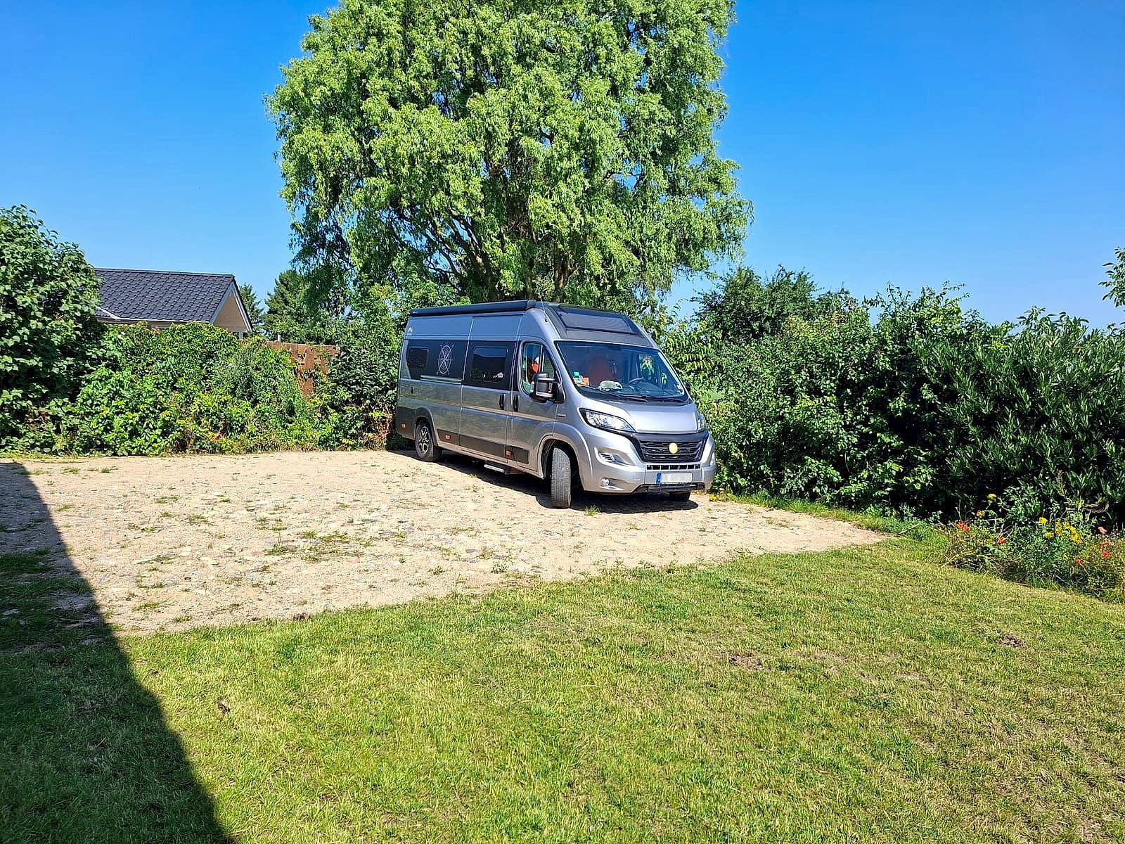 Wohnmobil auf dem leicht befestigten Stellplatz direkt an der Galerie HAUS HOPPE, dahinter ein großer Baum und offene Landschaft
