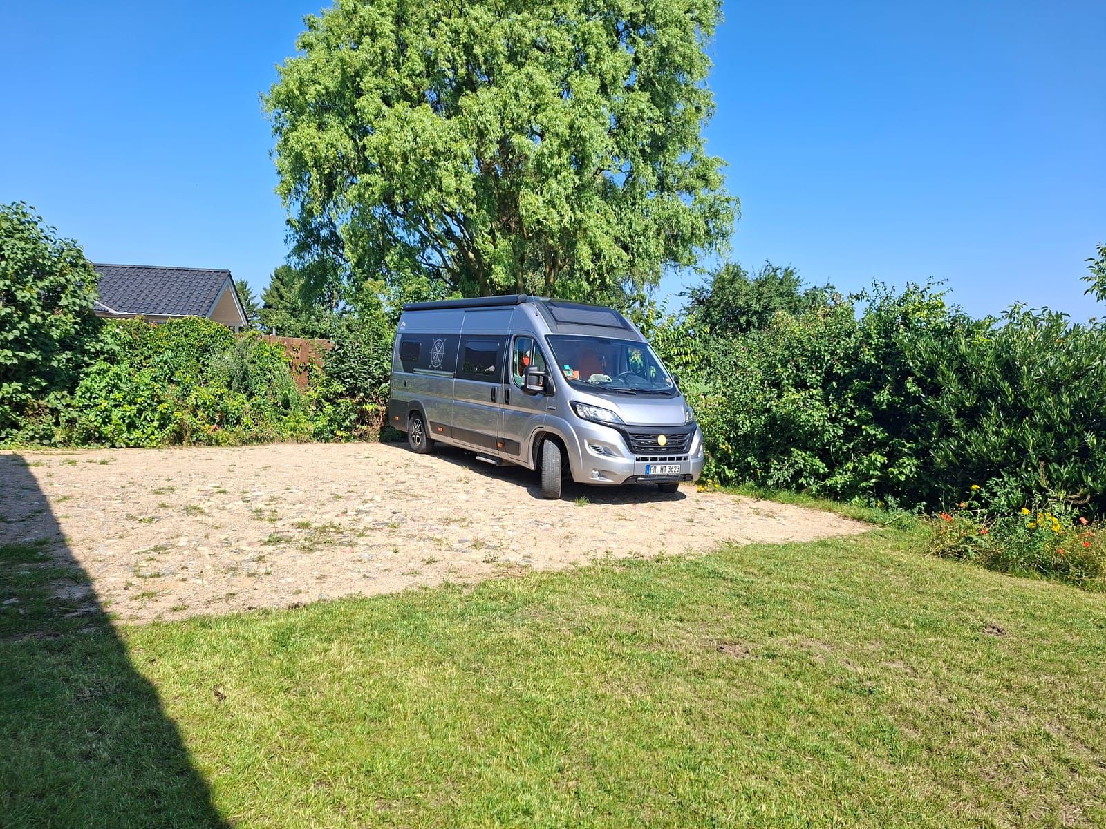 Wohnmobil auf dem leicht befestigten Stellplatz direkt an der Galerie HAUS HOPPE, dahinter ein großer Baum und offene Landschaft