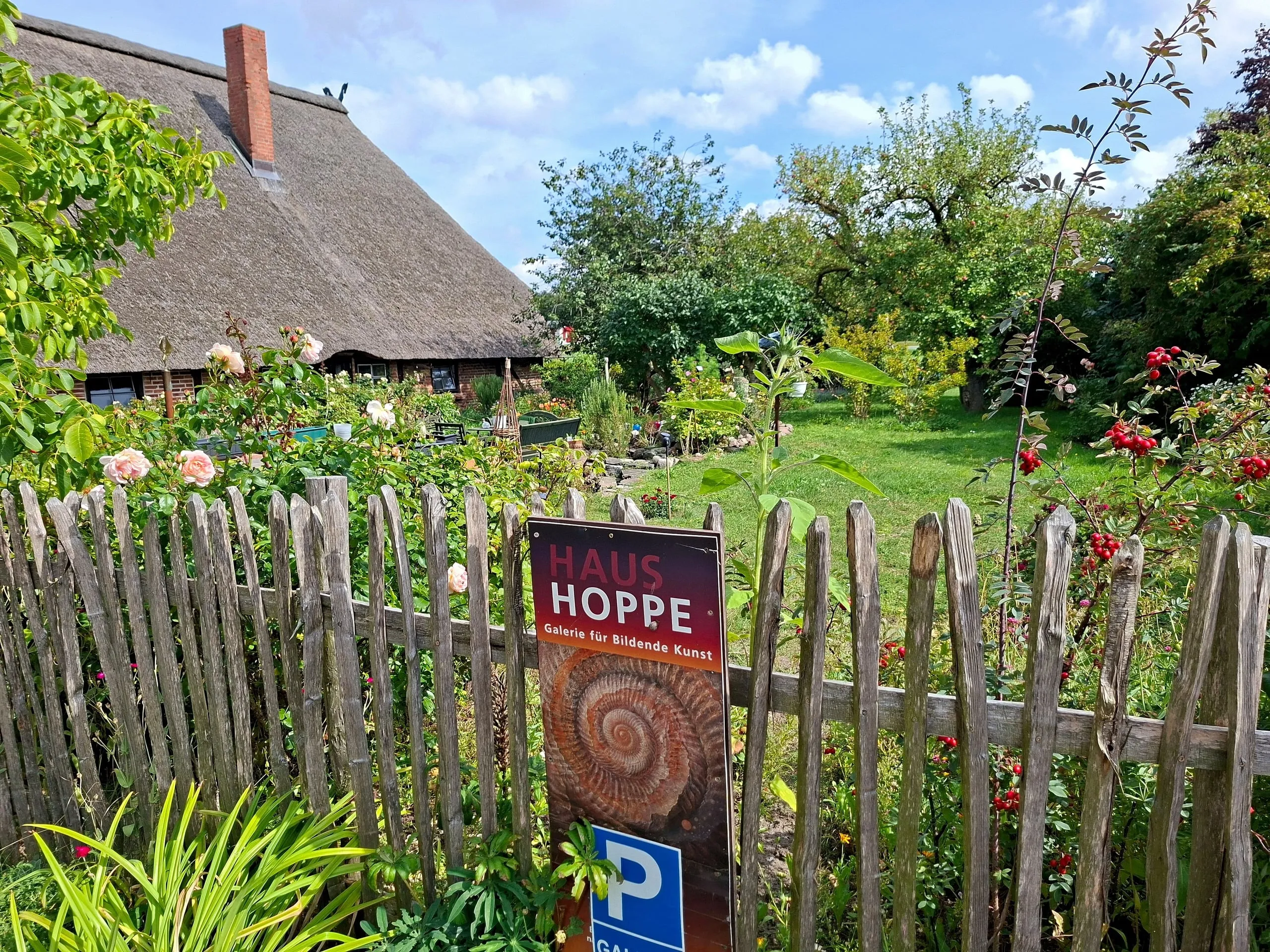 Rosen und Stauden im Bauerngarten, davor das Schild der Galerie HAUS HOPPE