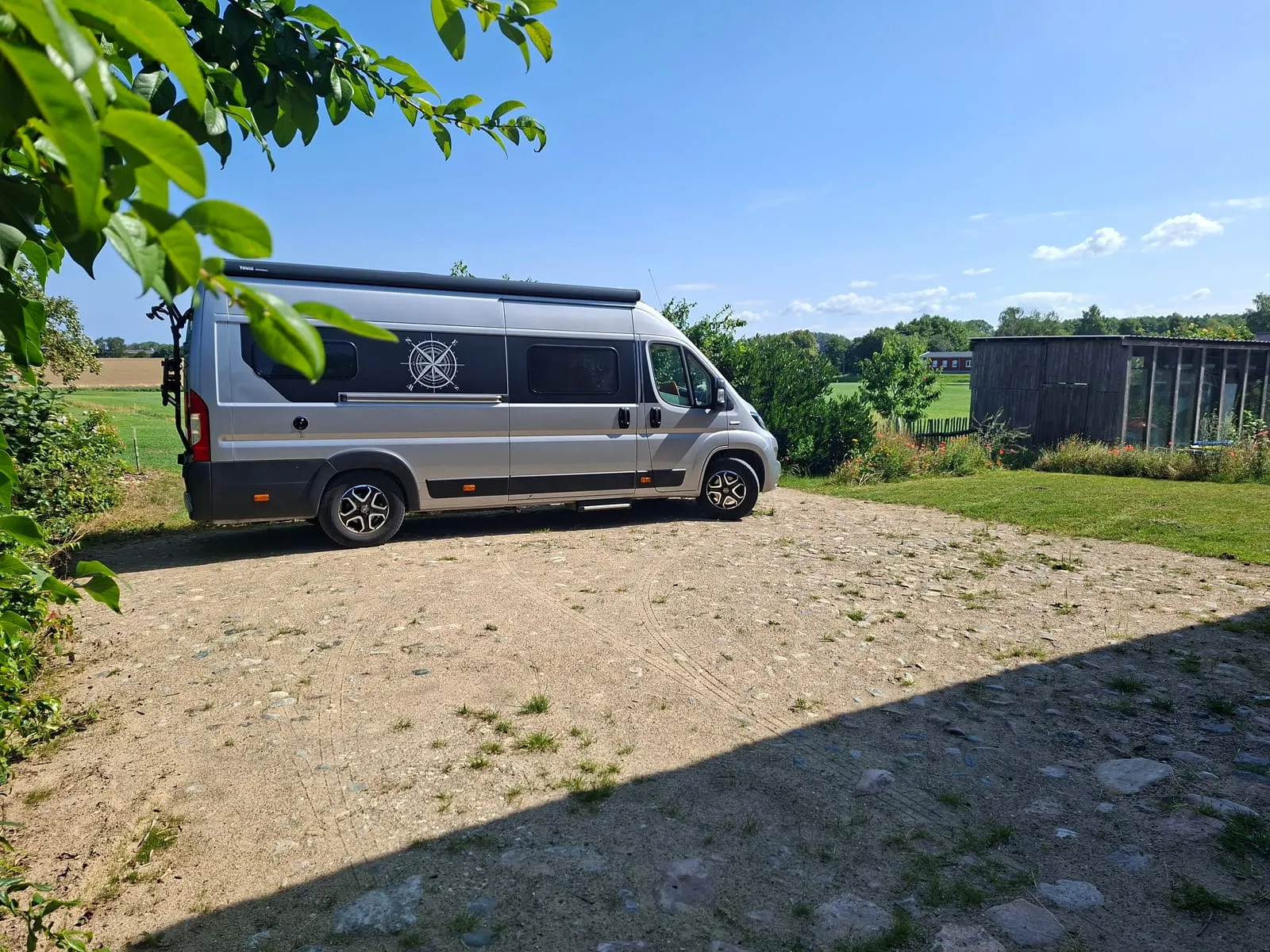 Wohnmobil auf dem Stellplatz, dahinter Bäume und offene Landschaft