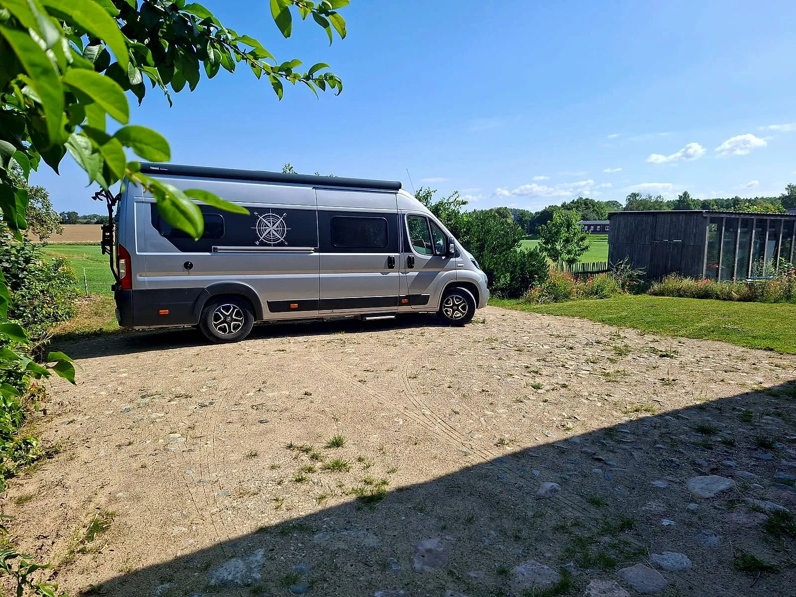 Wohnmobil auf dem Stellplatz, dahinter Bäume und offene Landschaft